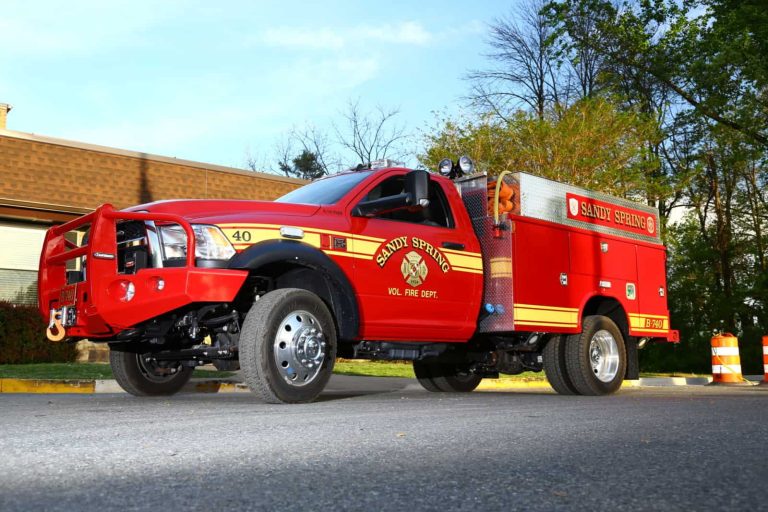 Brush 740 Sandy Spring VFD truck parked outside, with trees and a brick building in the background, photographed from a low angle on a sunny day.